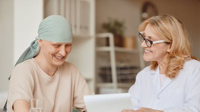 Warm-toned portrait of smiling bald woman listening to female doctor showing negative test results during consultation on alopecia and cancer recovery, copy space