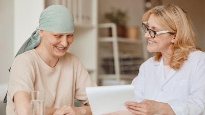 Warm-toned portrait of smiling bald woman listening to female doctor showing negative test results during consultation on alopecia and cancer recovery, copy space