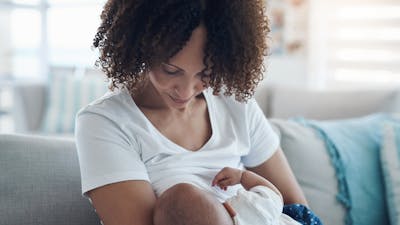 Shot of a young woman breastfeeding her adorable baby girl on the sofa at home.