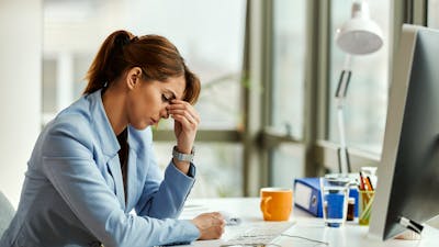 Young displeased businesswoman holding her head in pain while working in the office.