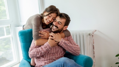Couple in love sitting in an armchair by the window, hugging and enjoying their time together