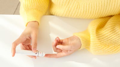 Glucometer in female hands on light background, top view